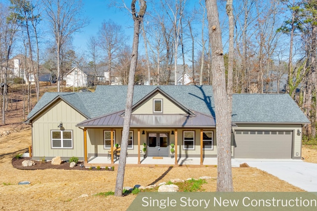 view of front of house featuring french doors, a porch, a shingled roof, concrete driveway, and a standing seam roof