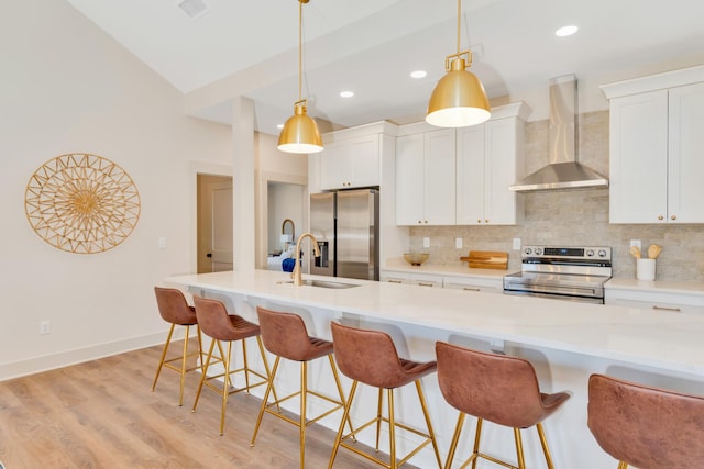 kitchen featuring light wood finished floors, appliances with stainless steel finishes, backsplash, wall chimney range hood, and a sink