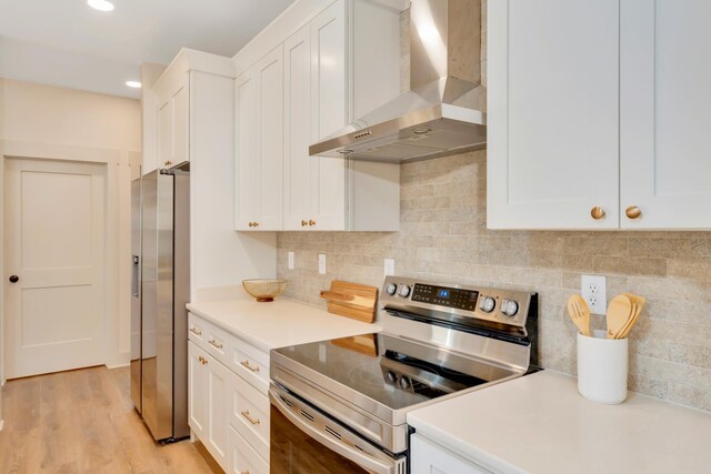 kitchen with backsplash, light wood-style flooring, appliances with stainless steel finishes, white cabinets, and wall chimney exhaust hood