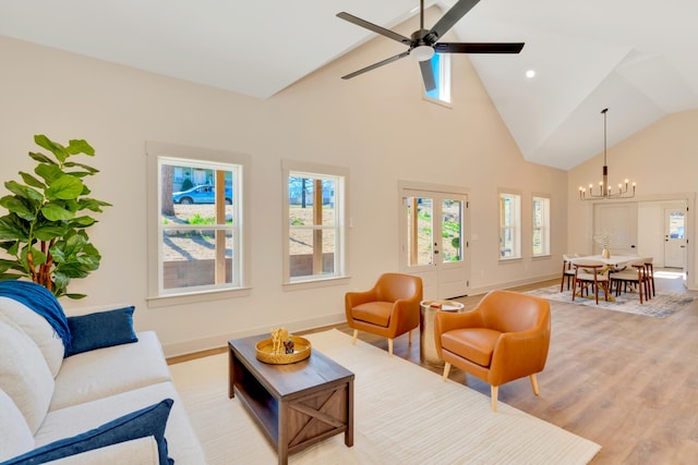 living room with ceiling fan with notable chandelier, high vaulted ceiling, light wood-style flooring, and baseboards