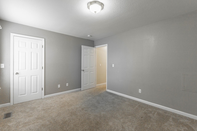 unfurnished bedroom with a textured ceiling, carpet floors, visible vents, and baseboards