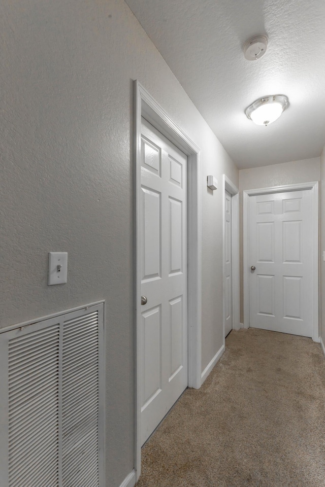 hallway featuring baseboards, visible vents, a textured wall, a textured ceiling, and carpet floors