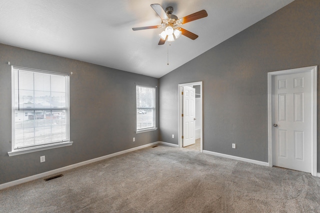 carpeted empty room featuring baseboards, visible vents, vaulted ceiling, and a ceiling fan