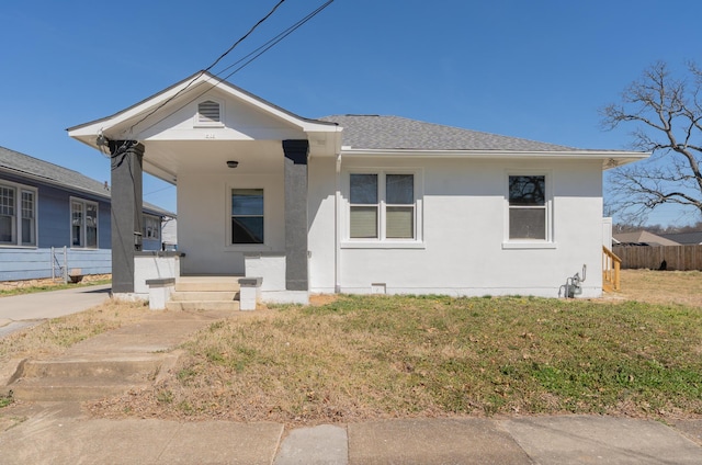 view of front of property featuring roof with shingles, stucco siding, covered porch, fence, and a front lawn