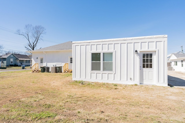 back of house with entry steps, a lawn, cooling unit, and board and batten siding