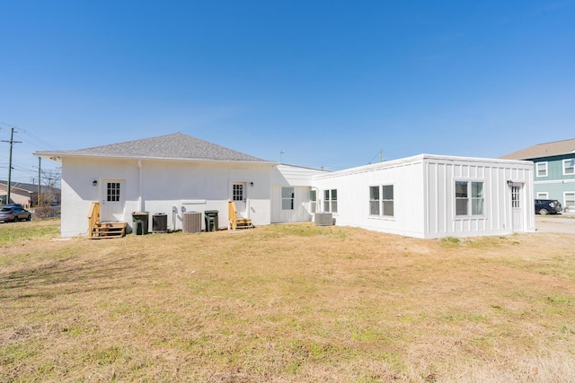 back of property featuring entry steps, roof with shingles, central AC, and a yard