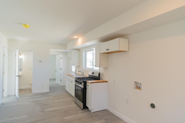 kitchen with light wood finished floors, baseboards, white cabinets, butcher block counters, and stainless steel gas range