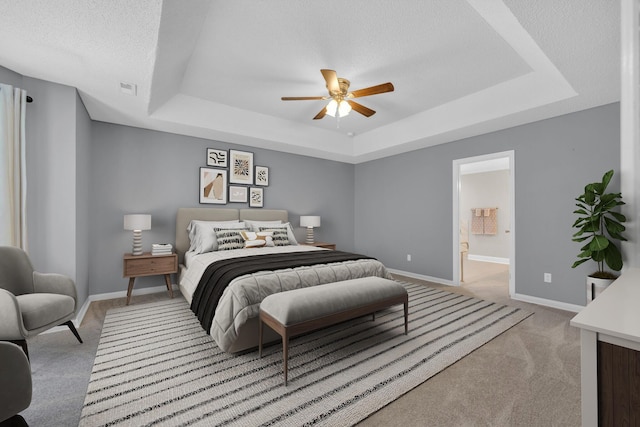 bedroom with a textured ceiling, a tray ceiling, carpet flooring, and baseboards