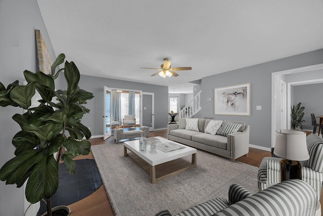 living room featuring stairs, ceiling fan, baseboards, and wood finished floors