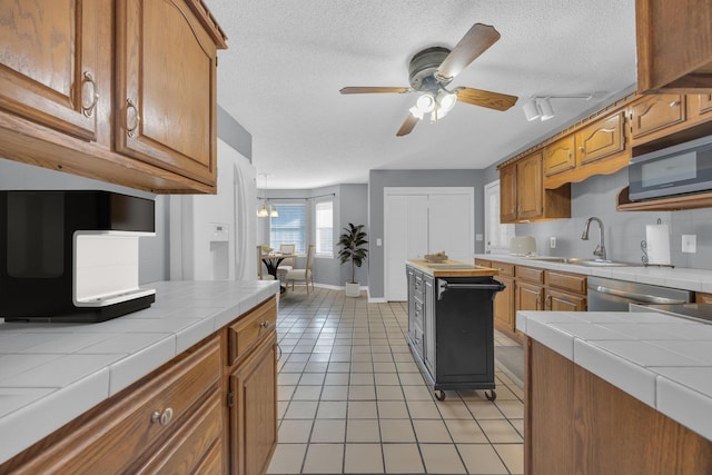 kitchen featuring light tile patterned floors, tile counters, appliances with stainless steel finishes, a sink, and a textured ceiling