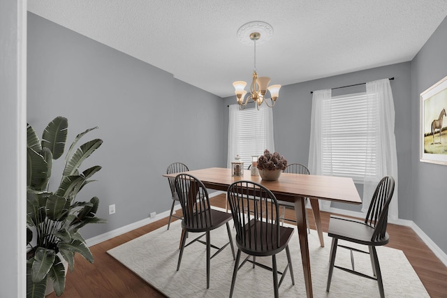 dining space with baseboards, a textured ceiling, a chandelier, and wood finished floors