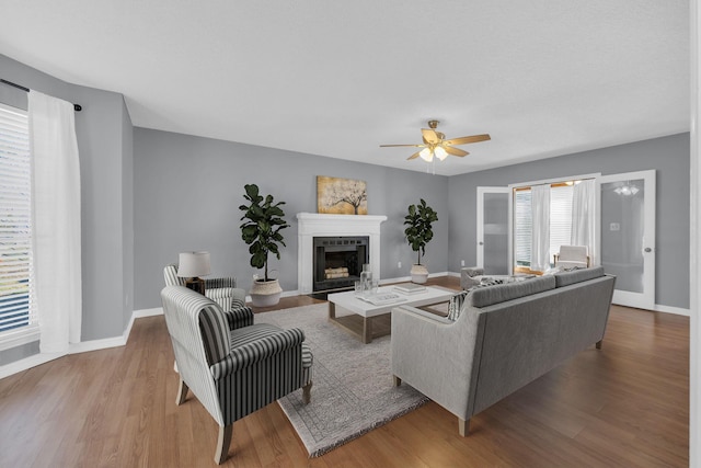 living area with a ceiling fan, a fireplace with flush hearth, baseboards, and wood finished floors