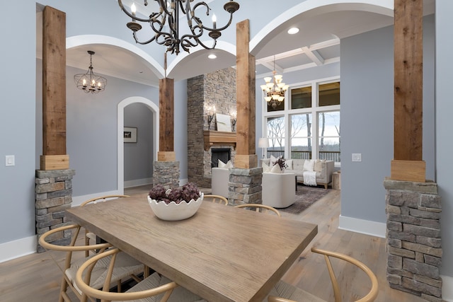 dining area with baseboards, coffered ceiling, light wood-style flooring, a fireplace, and a chandelier