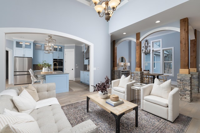 living area with arched walkways, recessed lighting, a towering ceiling, light wood-type flooring, and an inviting chandelier