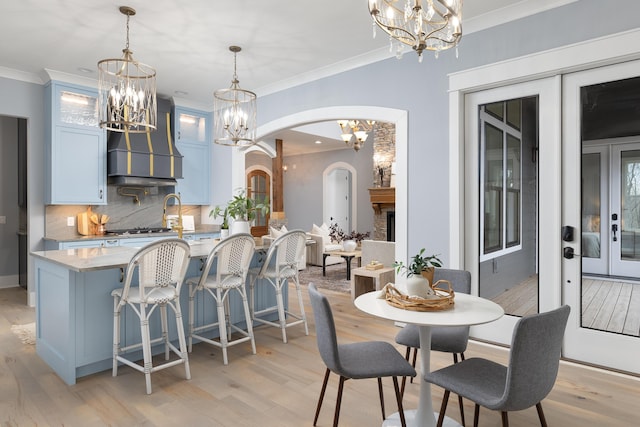 dining area with arched walkways, an inviting chandelier, crown molding, french doors, and light wood-type flooring