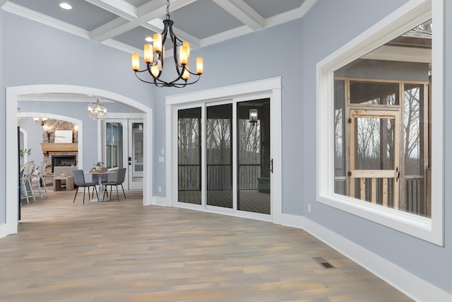 dining room featuring coffered ceiling, wood finished floors, a stone fireplace, a chandelier, and beam ceiling