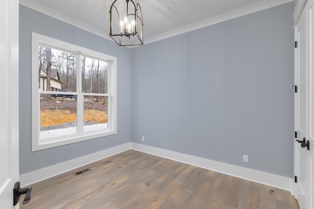 spare room featuring plenty of natural light, wood finished floors, and an inviting chandelier