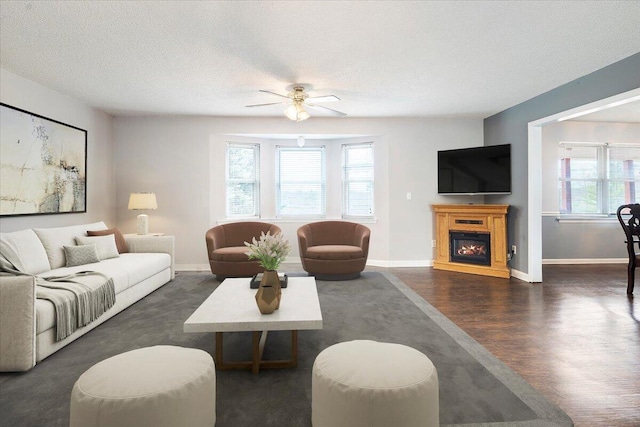 living room featuring ceiling fan, baseboards, wood finished floors, a glass covered fireplace, and a textured ceiling