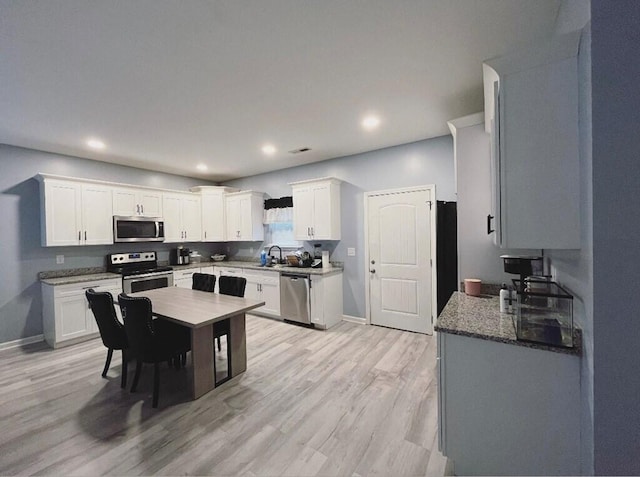 kitchen featuring stainless steel appliances, a sink, white cabinetry, baseboards, and light wood-style floors