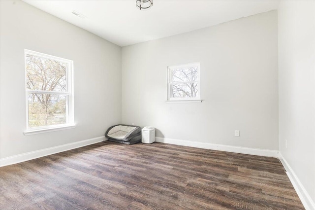 empty room featuring a wealth of natural light, baseboards, and dark wood finished floors