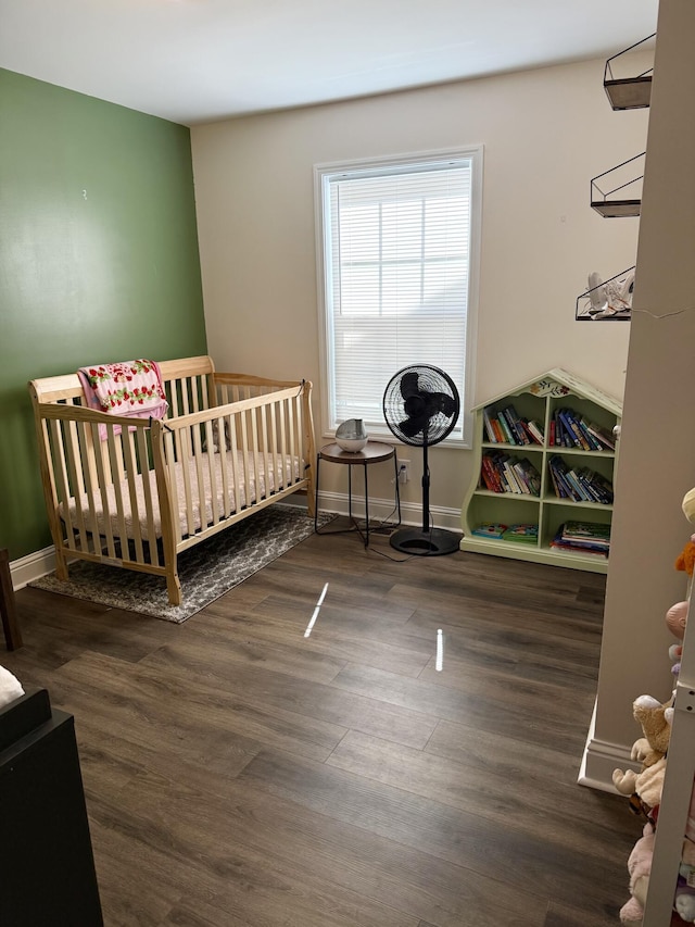 bedroom with baseboards, a crib, and wood finished floors