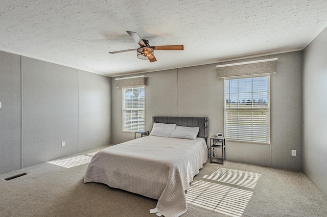 bedroom featuring a textured ceiling, carpet floors, visible vents, and a ceiling fan