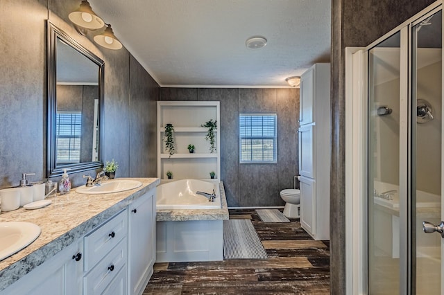 full bath featuring double vanity, a stall shower, toilet, wood finished floors, and a sink