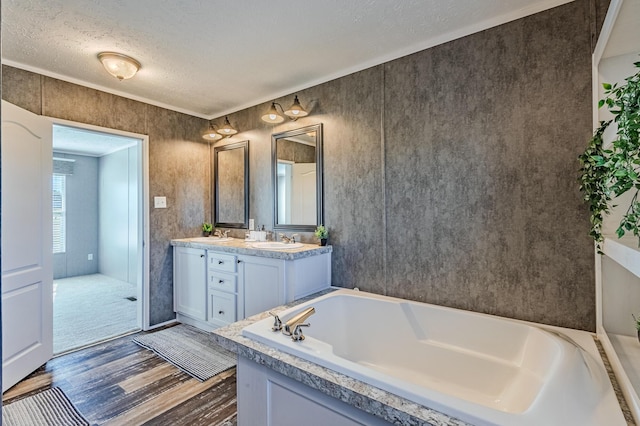 full bath with double vanity, a sink, a textured ceiling, wood finished floors, and a bath