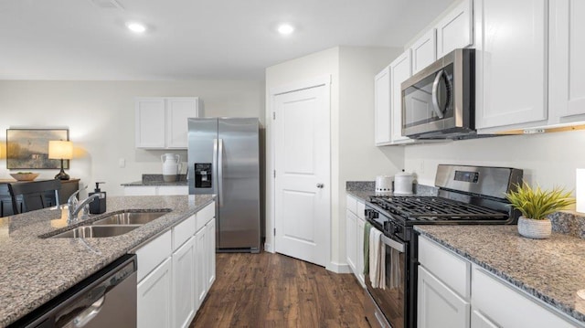 kitchen with white cabinets, dark wood finished floors, light stone counters, appliances with stainless steel finishes, and a sink