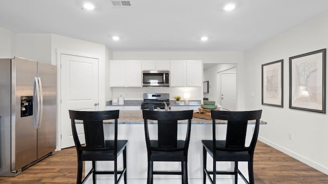 kitchen featuring a breakfast bar area, stainless steel appliances, dark wood-type flooring, white cabinets, and a center island with sink