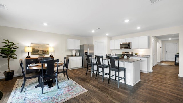 kitchen with a breakfast bar, dark wood-style flooring, white cabinets, appliances with stainless steel finishes, and a center island