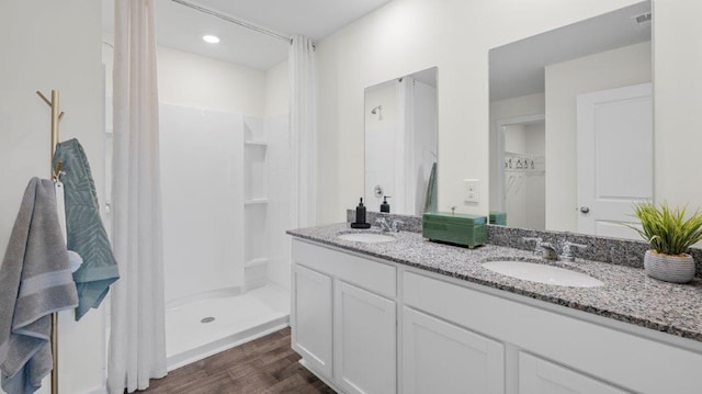 bathroom with double vanity, wood finished floors, a sink, and a shower stall