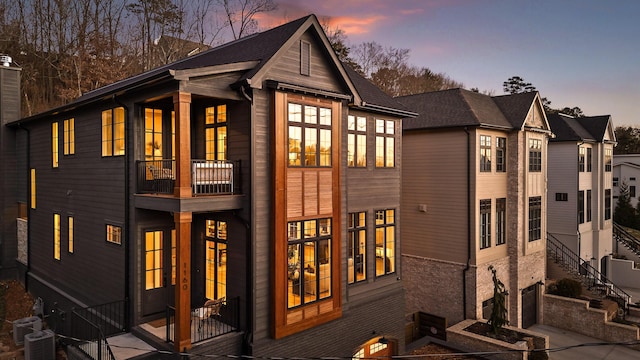 back of house at dusk featuring central AC, brick siding, a chimney, and a balcony