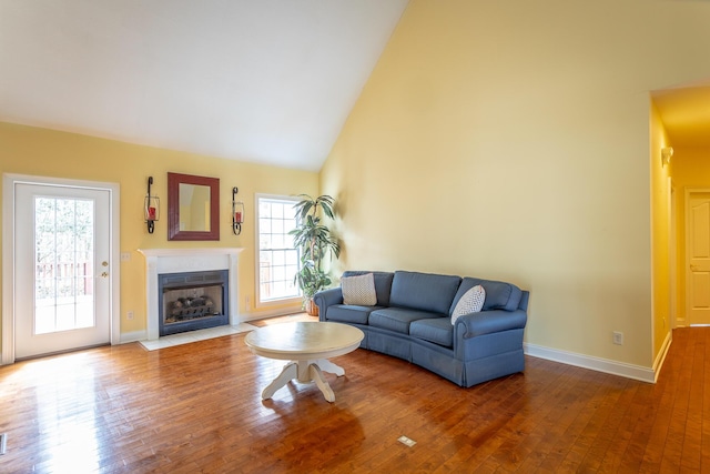 living room featuring baseboards, a fireplace with flush hearth, high vaulted ceiling, and hardwood / wood-style flooring