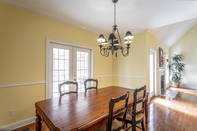 dining space with baseboards, a fireplace with flush hearth, french doors, wood-type flooring, and crown molding