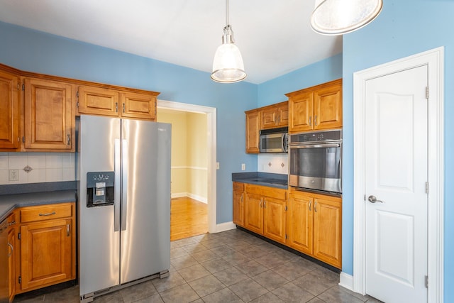 kitchen with backsplash, dark countertops, stainless steel appliances, brown cabinetry, and hanging light fixtures