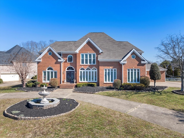 view of front facade featuring brick siding, curved driveway, a front yard, and a shingled roof