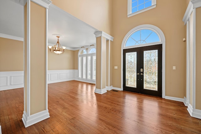 foyer featuring crown molding, french doors, wood finished floors, a notable chandelier, and ornate columns