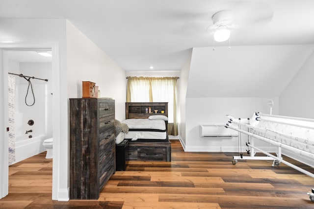 bedroom with ensuite bathroom, a wall mounted AC, wood finished floors, and baseboards