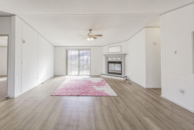 unfurnished living room featuring light wood-type flooring, ceiling fan, and a tiled fireplace