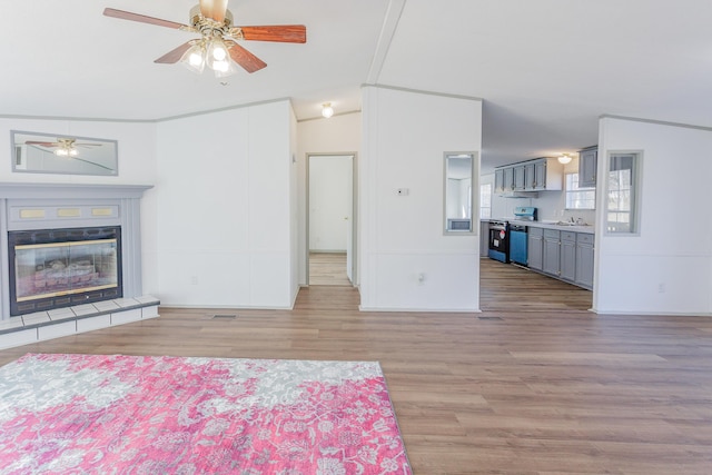 unfurnished bedroom featuring lofted ceiling, a tiled fireplace, a sink, and light wood-style flooring