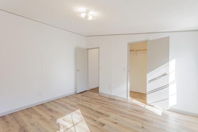 unfurnished bedroom featuring a closet, light wood-style flooring, and a spacious closet