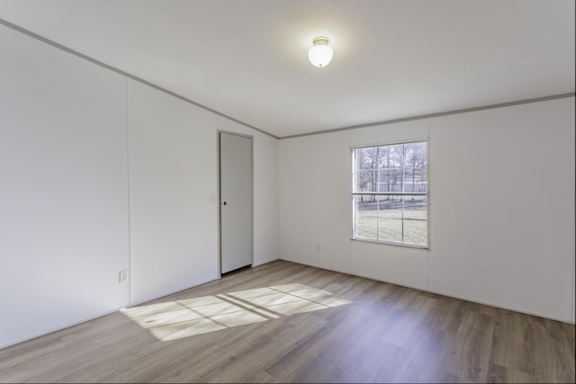 empty room with crown molding, vaulted ceiling, and wood finished floors