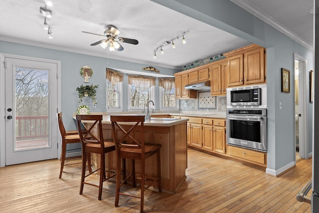 kitchen featuring crown molding, stainless steel appliances, light countertops, a sink, and under cabinet range hood