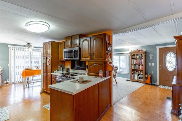 kitchen featuring a ceiling fan, brown cabinets, a peninsula, stainless steel appliances, and light countertops