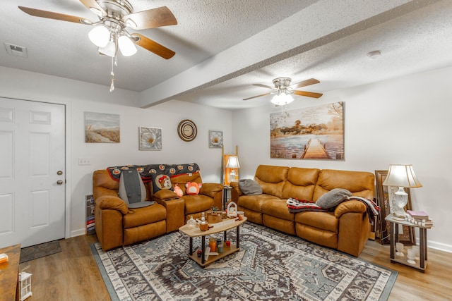 living room with a ceiling fan, visible vents, light wood-style flooring, and a textured ceiling