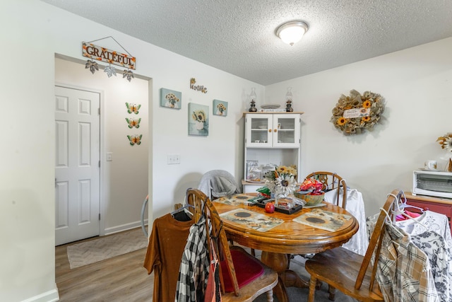 dining space featuring a textured ceiling, baseboards, and wood finished floors