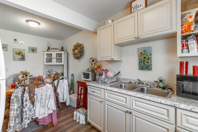 kitchen featuring a textured ceiling, black microwave, wood finished floors, a sink, and light countertops