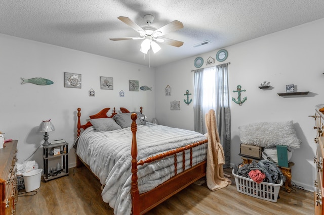 bedroom featuring a ceiling fan, a textured ceiling, visible vents, and wood finished floors