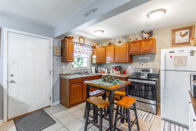 kitchen featuring light tile patterned floors, stainless steel electric range oven, brown cabinets, and freestanding refrigerator